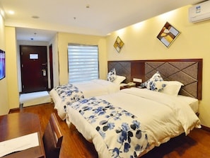 Une chambre d’hôtel avec deux lits, un bureau en bois, un téléphone et une fenêtre avec des stores.