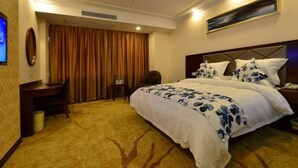 Habitación de hotel con una cama grande, un escritorio, una silla, un televisor y un cuadro en la pared.