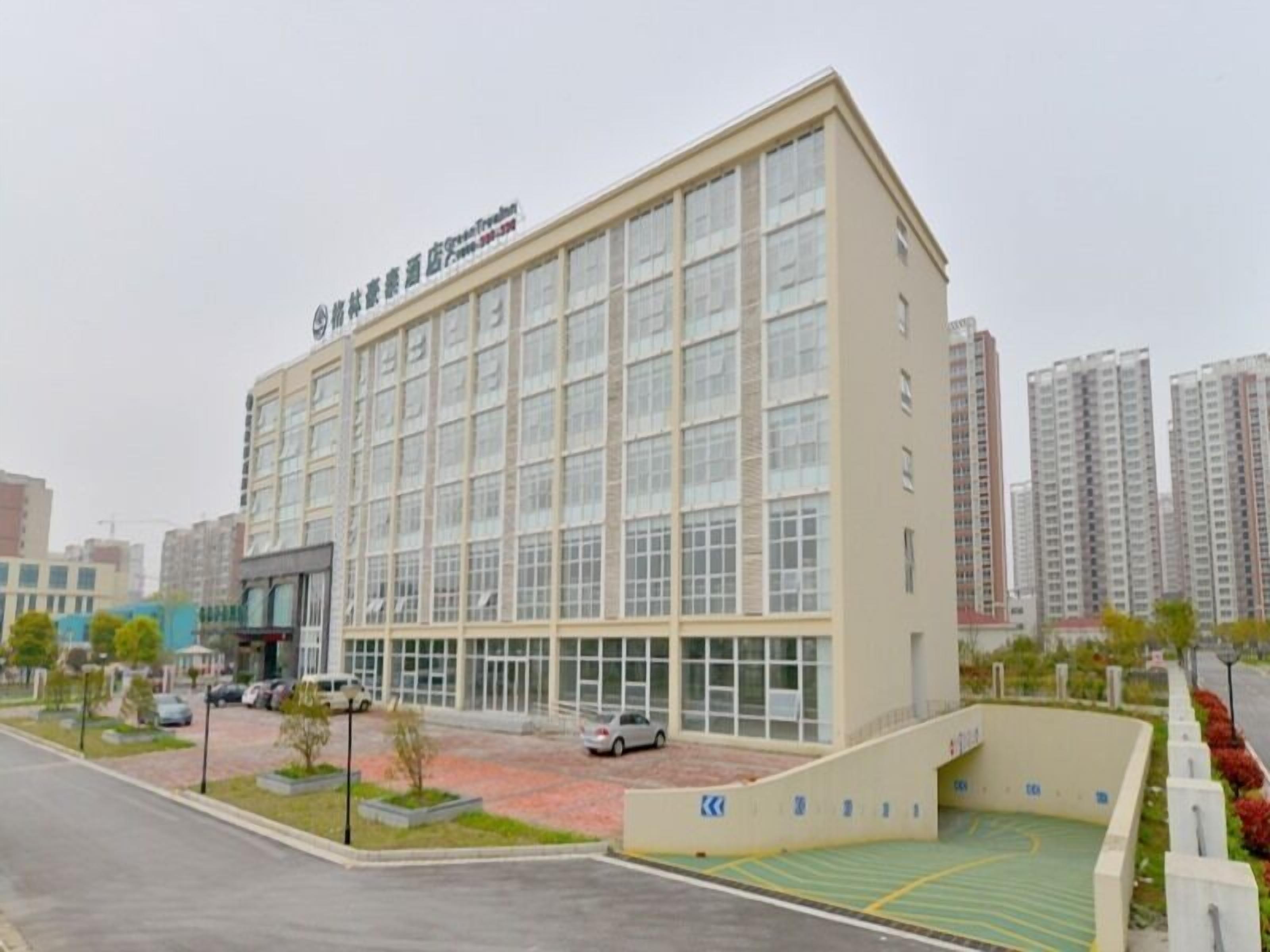 A multi-story building with a flat facade, large windows, and a parking area with a green sports court.