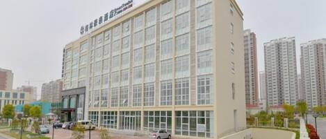 A multi-story building with a flat facade, large windows, and a parking area with a green sports court.