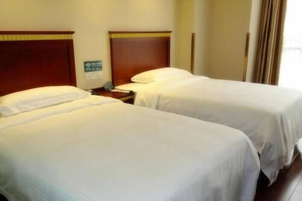 Une chambre d’hôtel avec deux lits, des têtes de lit en bois, une table de chevet et un panneau vert sur le mur.