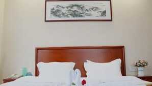 Une chambre d’hôtel avec une tête de lit en bois, deux oreillers blancs, un lit bien fait agrémenté d’une fleur rouge, une œuvre d’art encadrée au mur et une petite table sur laquelle est posé un vase de fleurs.