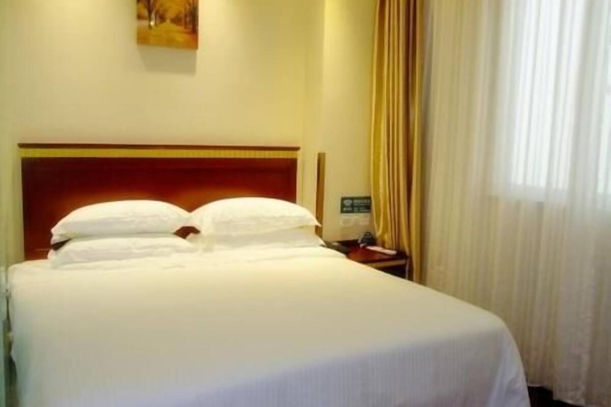 Une chambre d’hôtel avec un grand lit, une table de chevet, un tableau au mur et une fenêtre avec des rideaux.