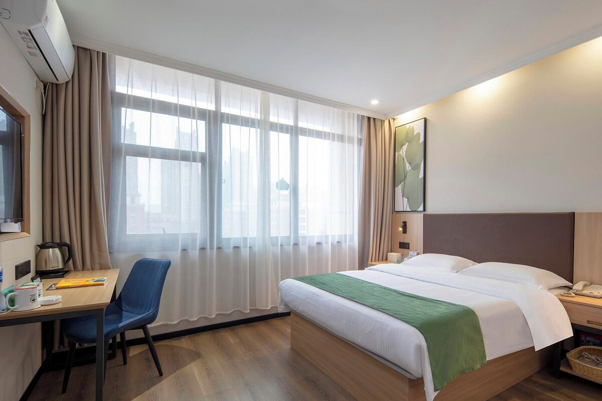 Een hotelkamer met een bed, een bureau met stoel, een koffiezetapparaat en een raam met gordijnen.