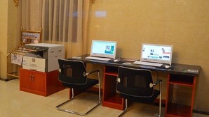 Une chambre d’hôtel avec deux bureaux, chacun équipé d’un ordinateur portable et d’une chaise. Il y a une imprimante et un petit meuble avec des papiers sur le côté gauche.
