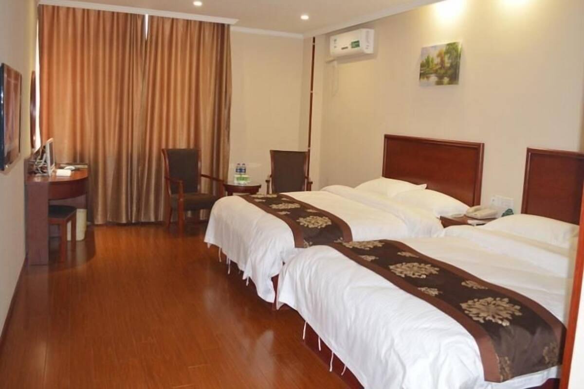 Une chambre d’hôtel avec deux lits, un bureau, une chaise, une bouteille d’eau et un appareil de climatisation.