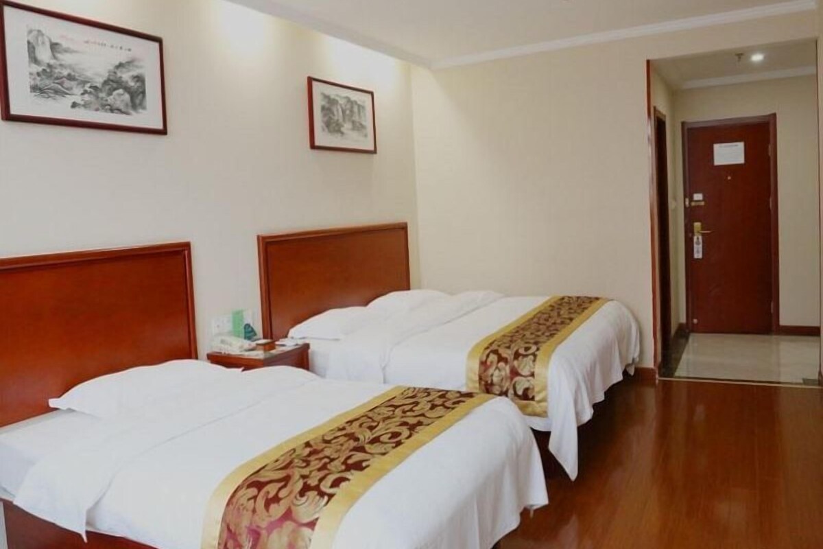 Een hotelkamer met twee bedden, houten hoofdeinden en een gang naar een deur.