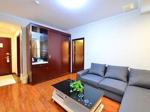 A modern living room with a sofa, a coffee table with a plant, wooden flooring, and a sliding door closet. - GreenTree Inn WuXi DongTing Leather City Express Hotel (Wuxi)