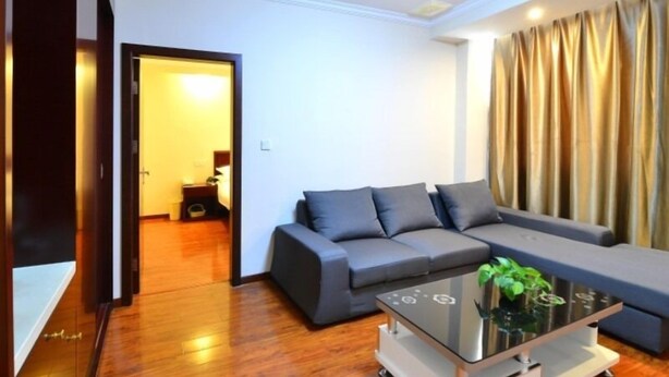 Uma sala de estar moderna com um sofá cinzento, uma mesa de centro de vidro e piso de madeira.