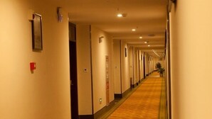 Um corredor de hotel comprido e estreito, com portas em ambos os lados, piso coberto de carpete e iluminação no teto.
