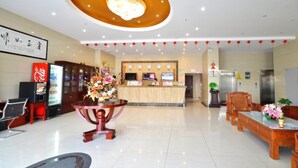 Um saguão de hotel com uma mesa de recepção, um refrigerador de Coca-Cola, um arranjo floral e uma área de atendimento em madeira.