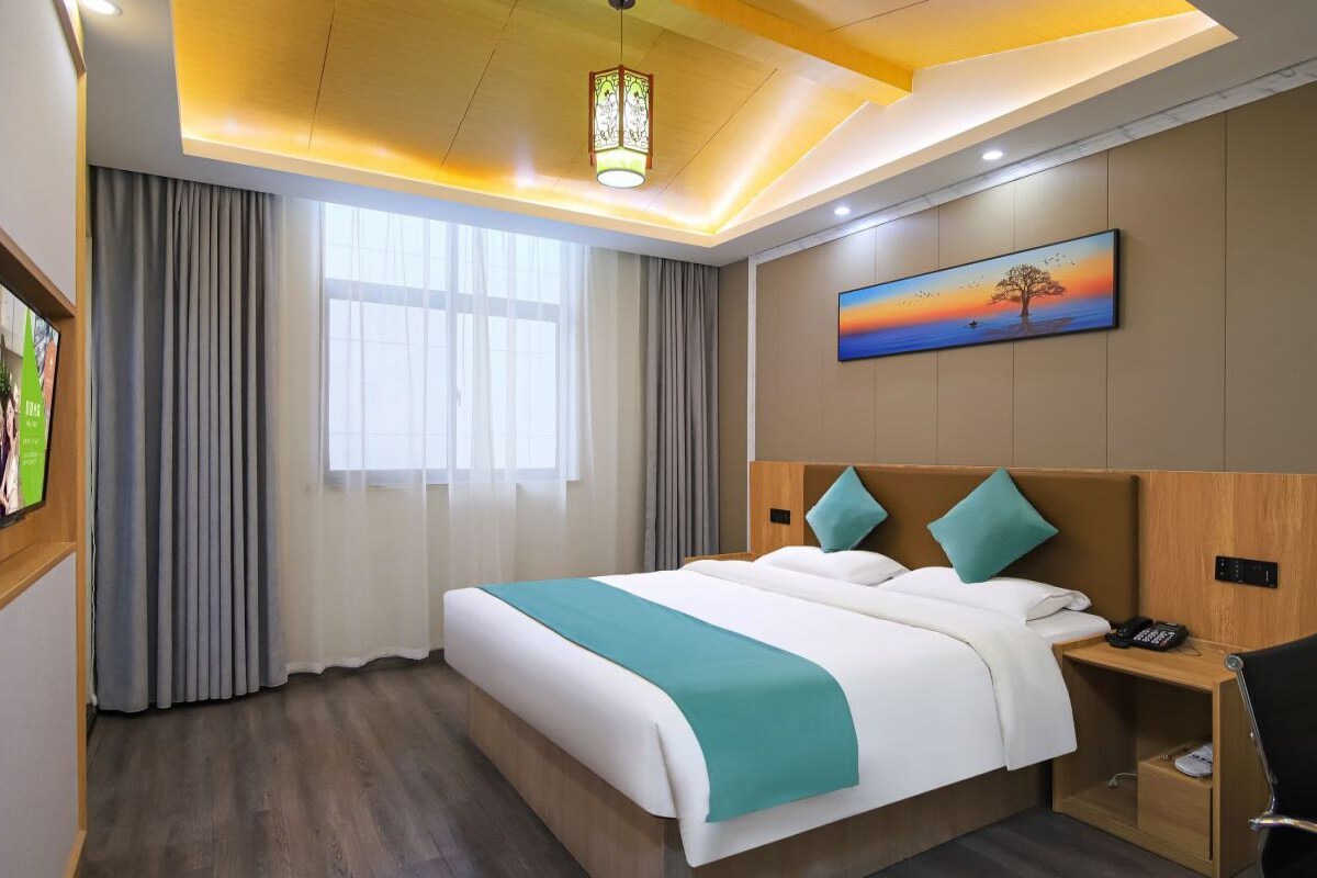 Une chambre d’hôtel avec un grand lit, un bureau avec une chaise, un tableau au mur et une fenêtre avec des rideaux.