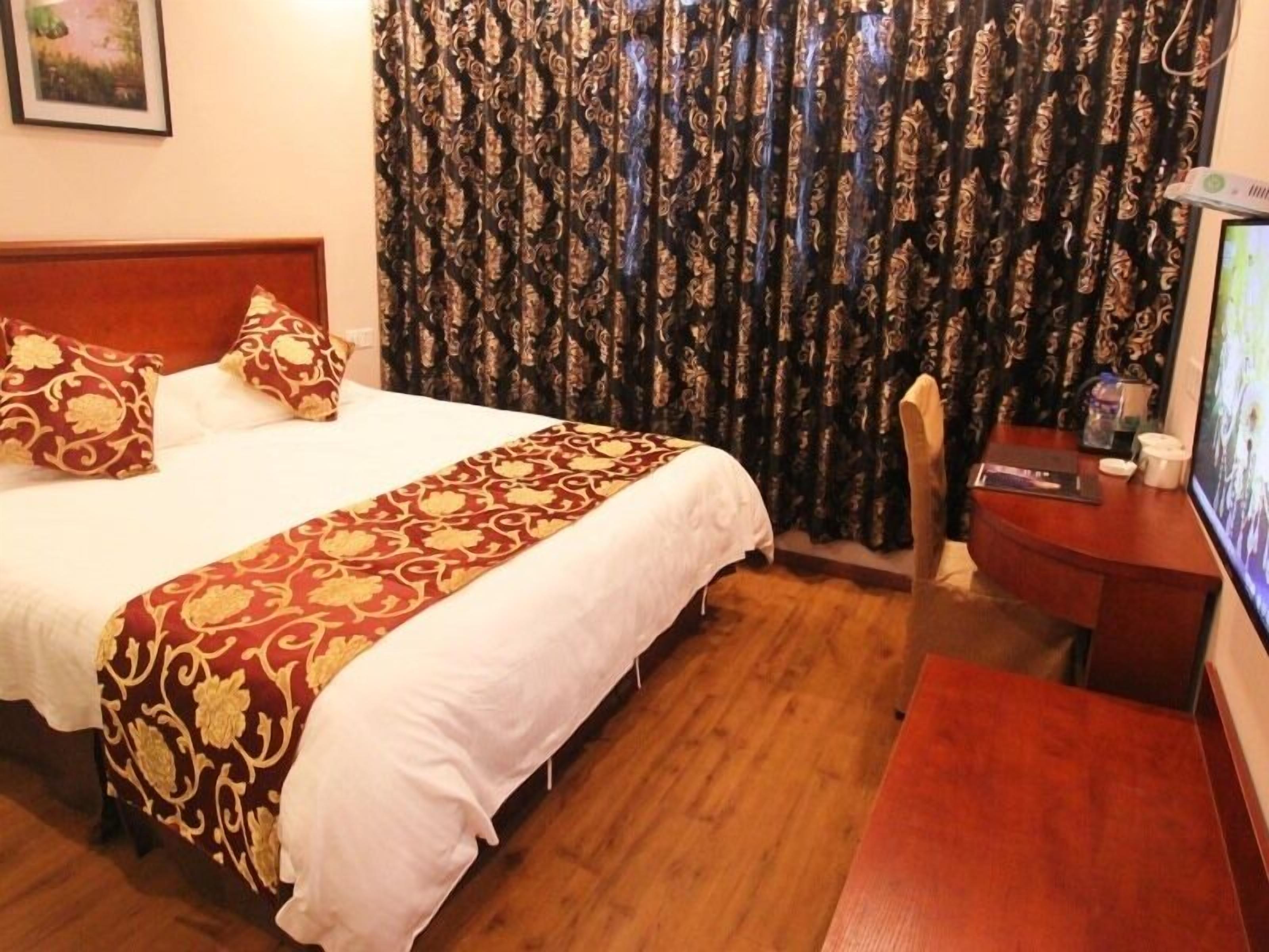 A hotel room with a bed, a wooden desk, a television, and curtains.