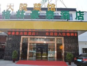 Ein Hotel Eingang mit rotem Teppich, Glasüren und einem Schild mit chinesischen Schriftzeichen.