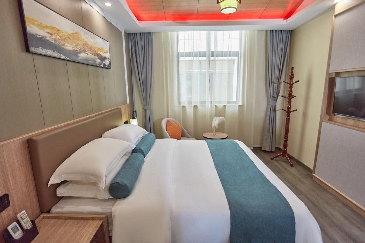 Une chambre d’hôtel avec un lit, une chaise, une télévision, un porte-manteau et une fenêtre avec des rideaux.