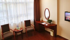 A hotel room with a wooden desk, two chairs, a small table with a plant, a mirror, and a television on the wall. - GreenTree Inn HanZhong Railway Station BeiYiHuan Road Express Hotel (Hanzhong)