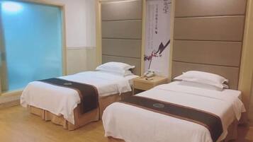 A hotel room with two beds, a bedside table, a nightstand, and a large window.