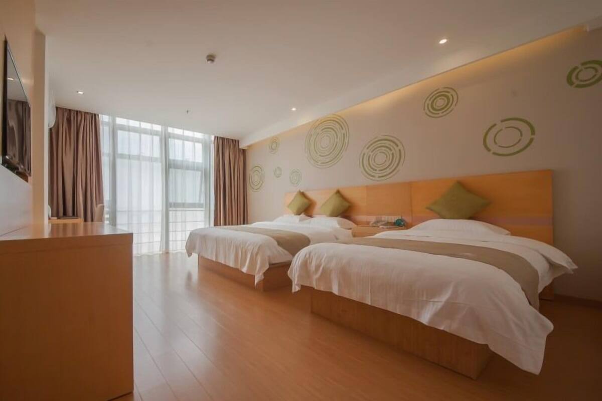 Ein Hotelzimmer mit zwei Betten, einem hölzernen Schminktisch und einem großen Fenster mit Vorhängen.