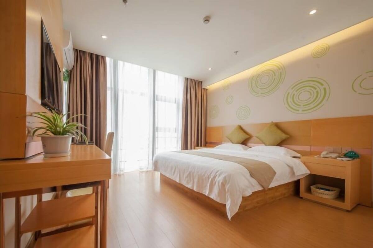 Ein modernes Hotelzimmer mit einem hölzernen Bett, einem Schreibtisch und einem großen Fenster mit Vorhängen.