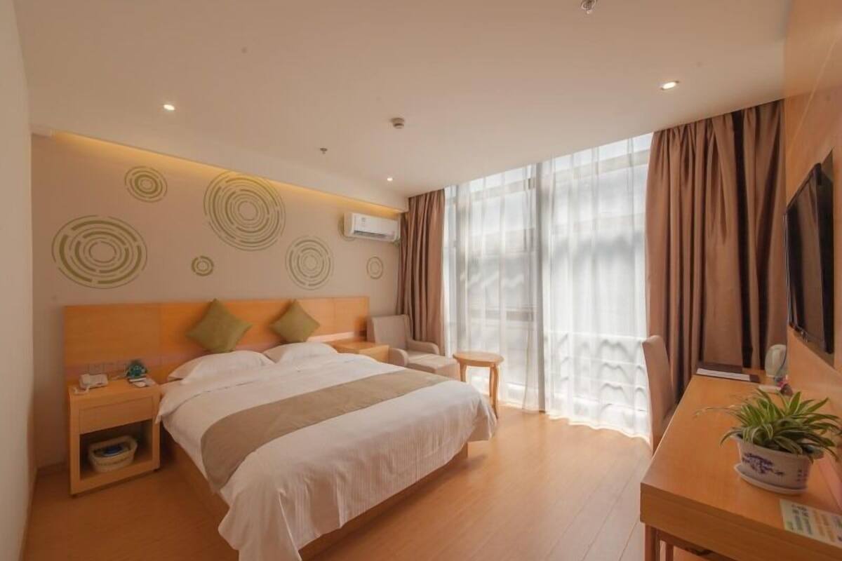 Ein Hotelzimmer mit einem großen Bett, Nachttischen, einem Schreibtisch mit Pflanze und einem Fernseher.