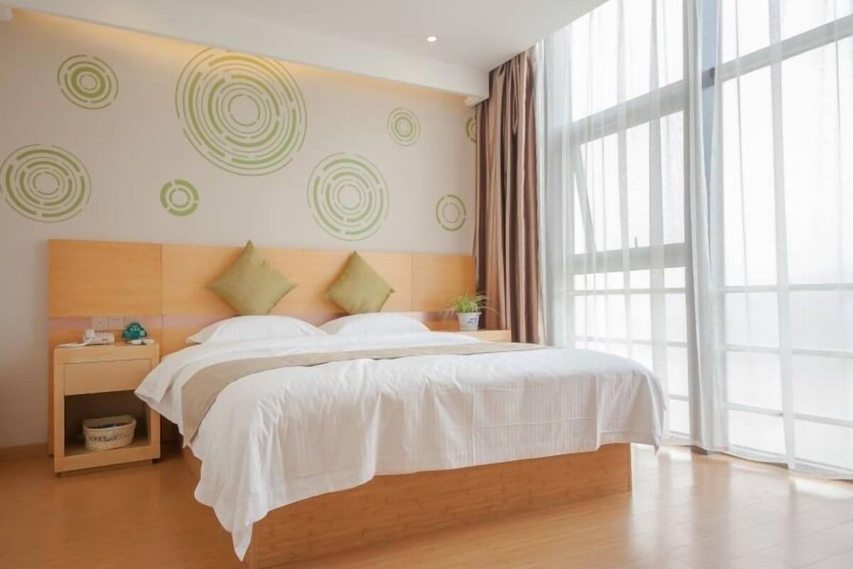 Ein modernes Hotelzimmer mit einem großen Bett, einem Holz-Kopfteil und einem Nachttisch mit Lampe.