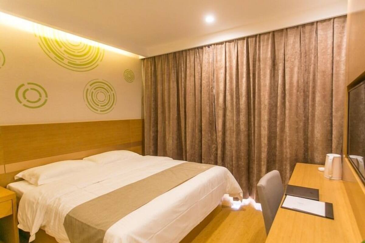 Une chambre d’hôtel avec un lit, un bureau, une chaise et une grande fenêtre avec des rideaux.
