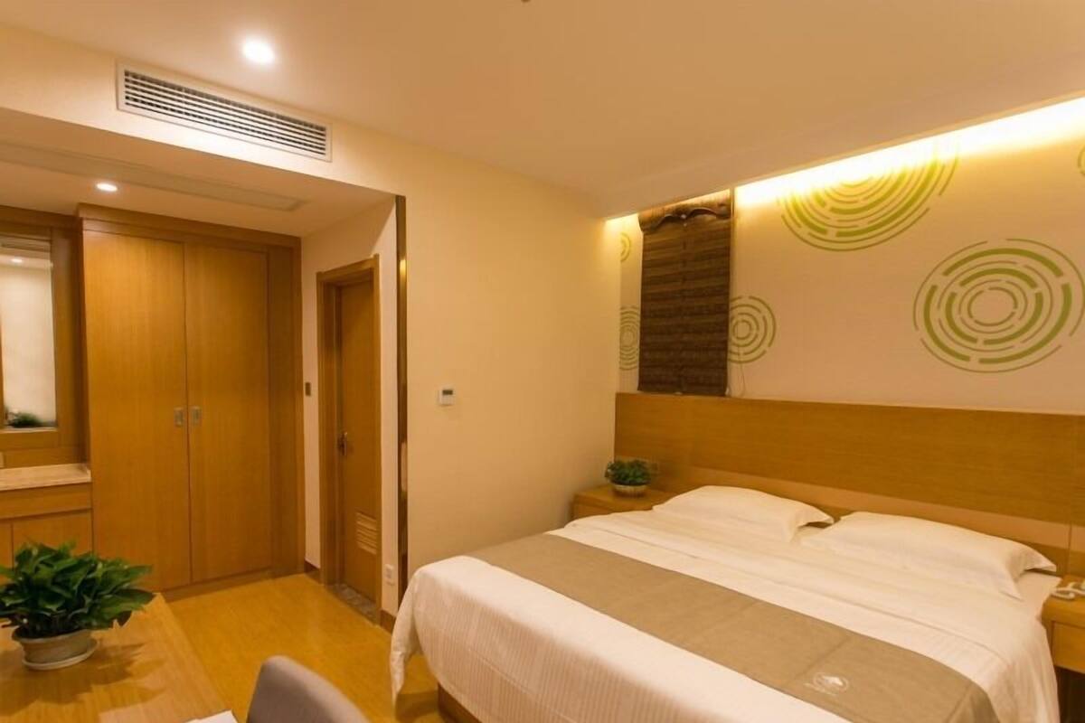 Une chambre d’hôtel comprenant un lit, un bureau, une chaise, une plante en pot et un mur orné de motifs circulaires.
