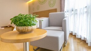 A modern hotel room with a grey sofa, a round wooden table with a plant, and a bed with a white headboard. - Greentree Inn (Suzhou)
