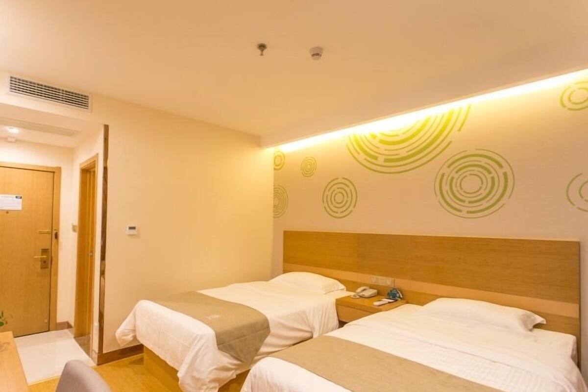 Une chambre d’hôtel avec deux lits, une tête de lit en bois, un bureau avec une chaise et un mur orné de motifs circulaires.