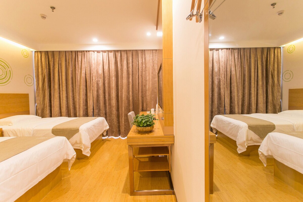 A hotel room with two beds, a wooden desk, a potted plant, and a mirror.