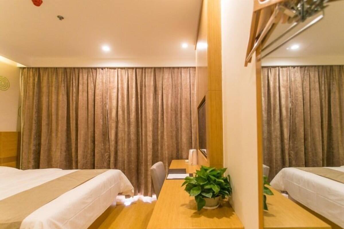 Une chambre d’hôtel avec deux lits, un bureau en bois, une chaise, une plante en pot et un miroir.