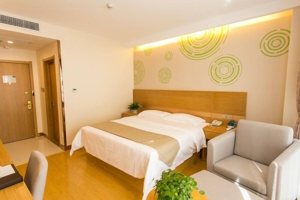 Une chambre d’hôtel comprenant un lit, un bureau, une chaise, une petite table avec une plante et un mur orné de motifs circulaires.