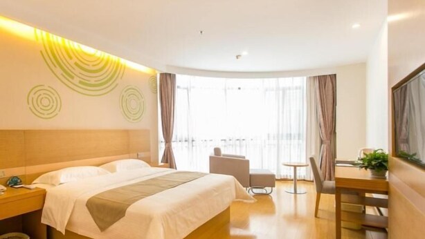 A hotel room with a large bed, a desk, and a chair. There is a window with curtains and a view of the outside. - Greentree Inn (Suzhou)