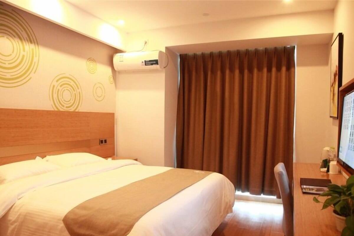 Ein Hotelzimmer mit Bett, Schreibtisch, Stuhl, Zimmerpflanze und einem fensterbepflanzten Fenster.