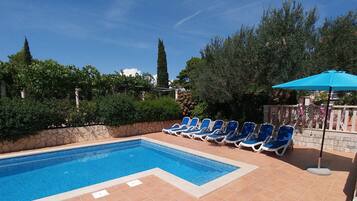 A swimming pool with blue tiles, surrounded by a stone wall and lush greenery.