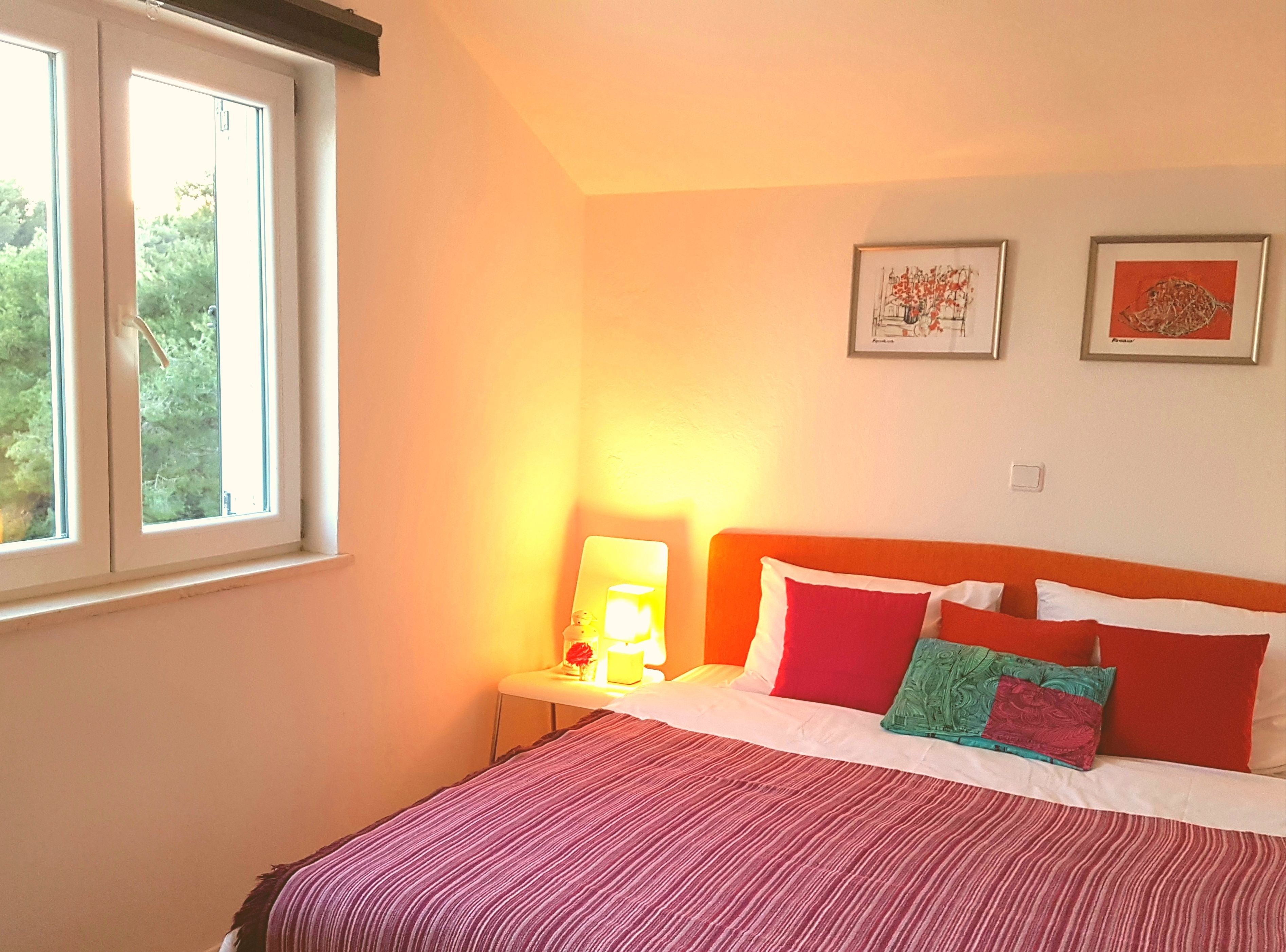 A bedroom with a bed, a nightstand, a lamp, and two framed pictures on the wall.