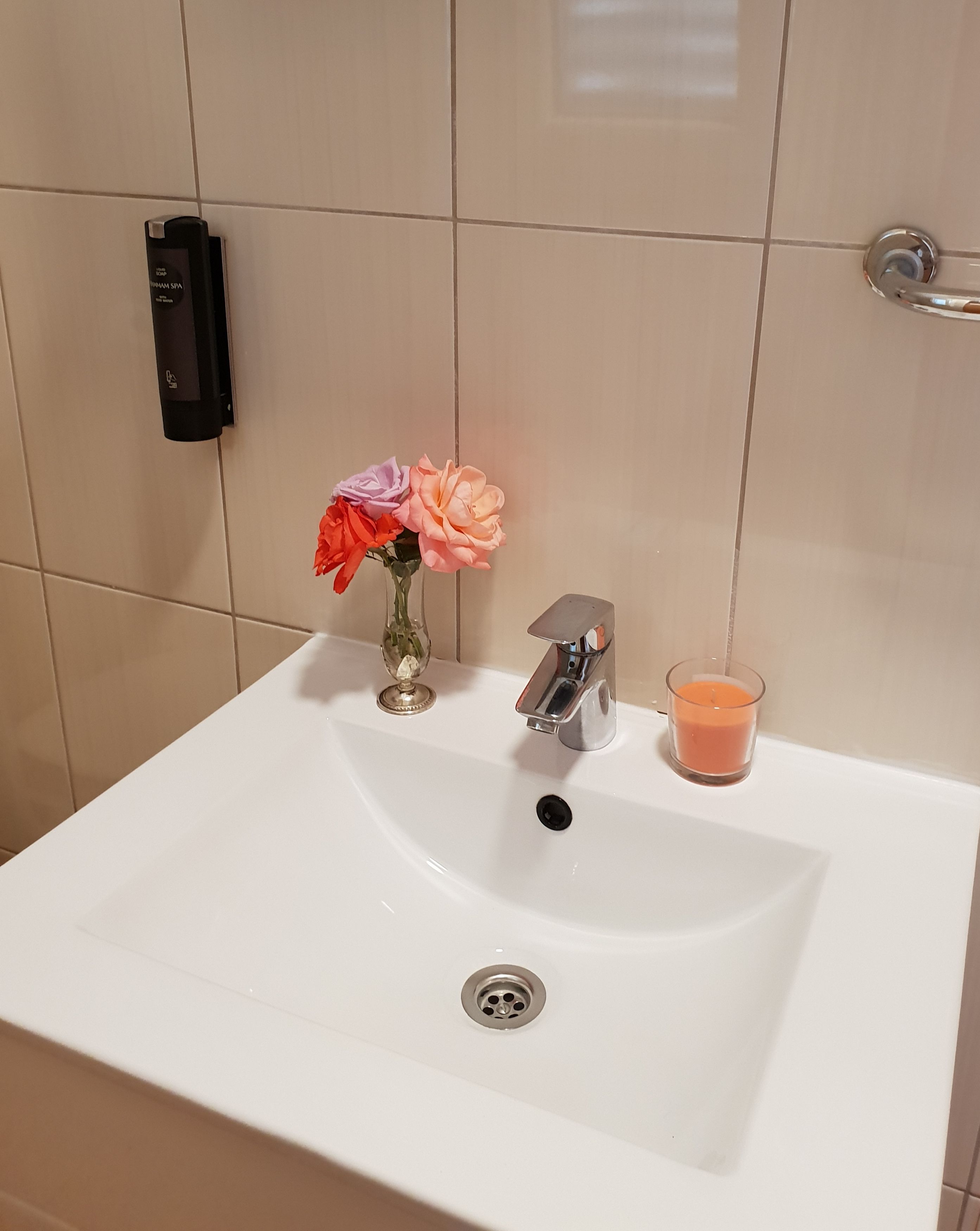 A bathroom sink with a modern faucet, a glass candle, and a vase with flowers.