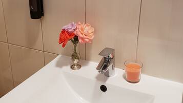 A bathroom sink with a modern faucet, a glass candle, and a vase with flowers.