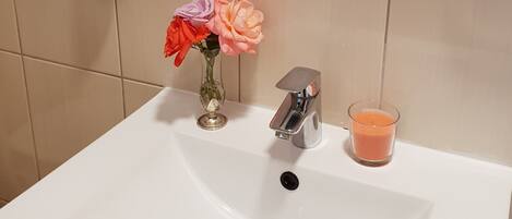 A bathroom sink with a modern faucet, a glass candle, and a vase with flowers.