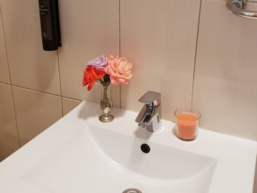 A bathroom sink with a modern faucet, a glass candle, and a vase with flowers.