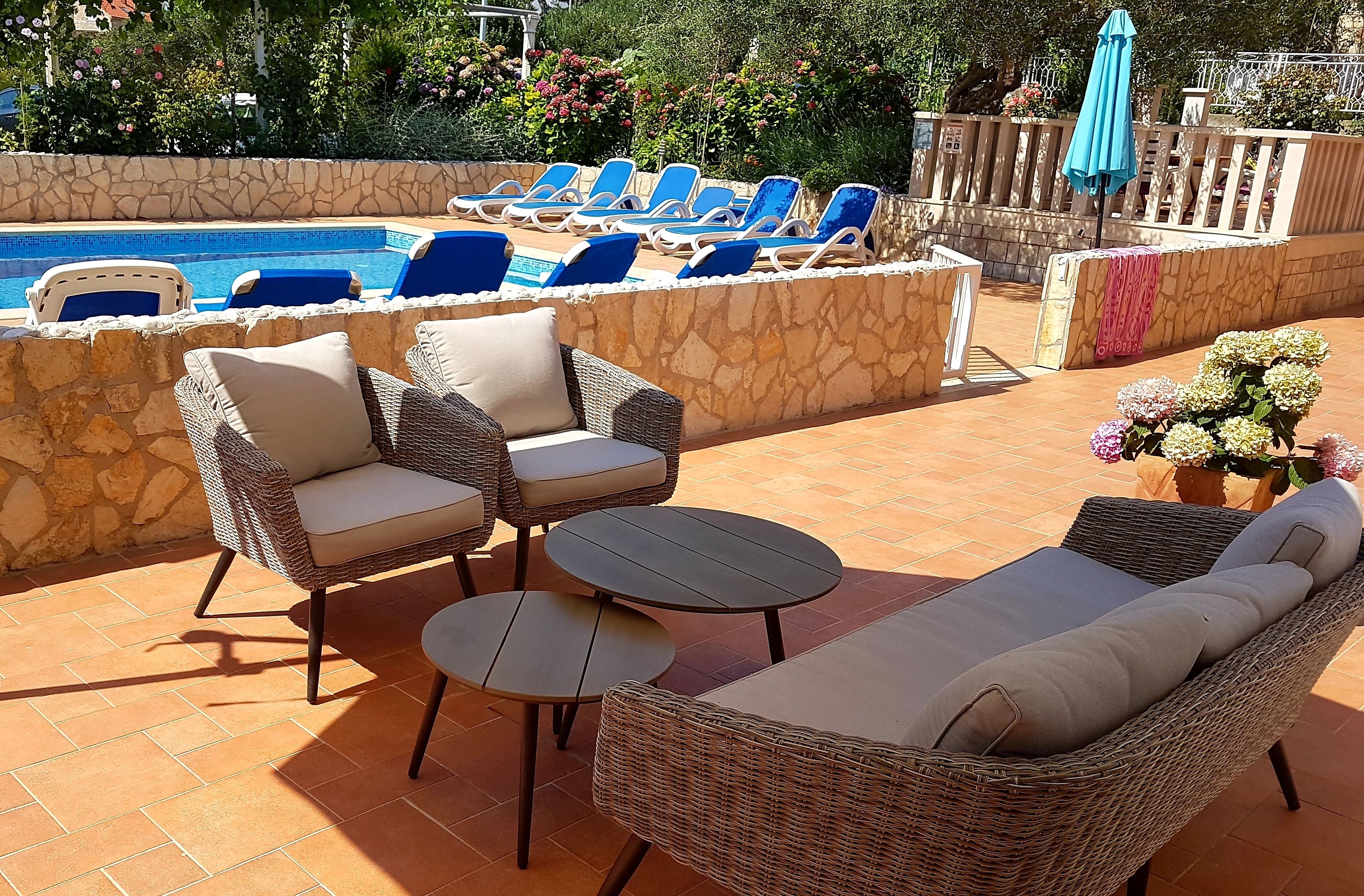 A poolside area with lounge chairs, a wicker sofa, and a small table.