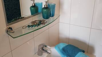 Un baño con lavamanos blanco, estante de vidrio con artículos de aseo y toalla azul.
