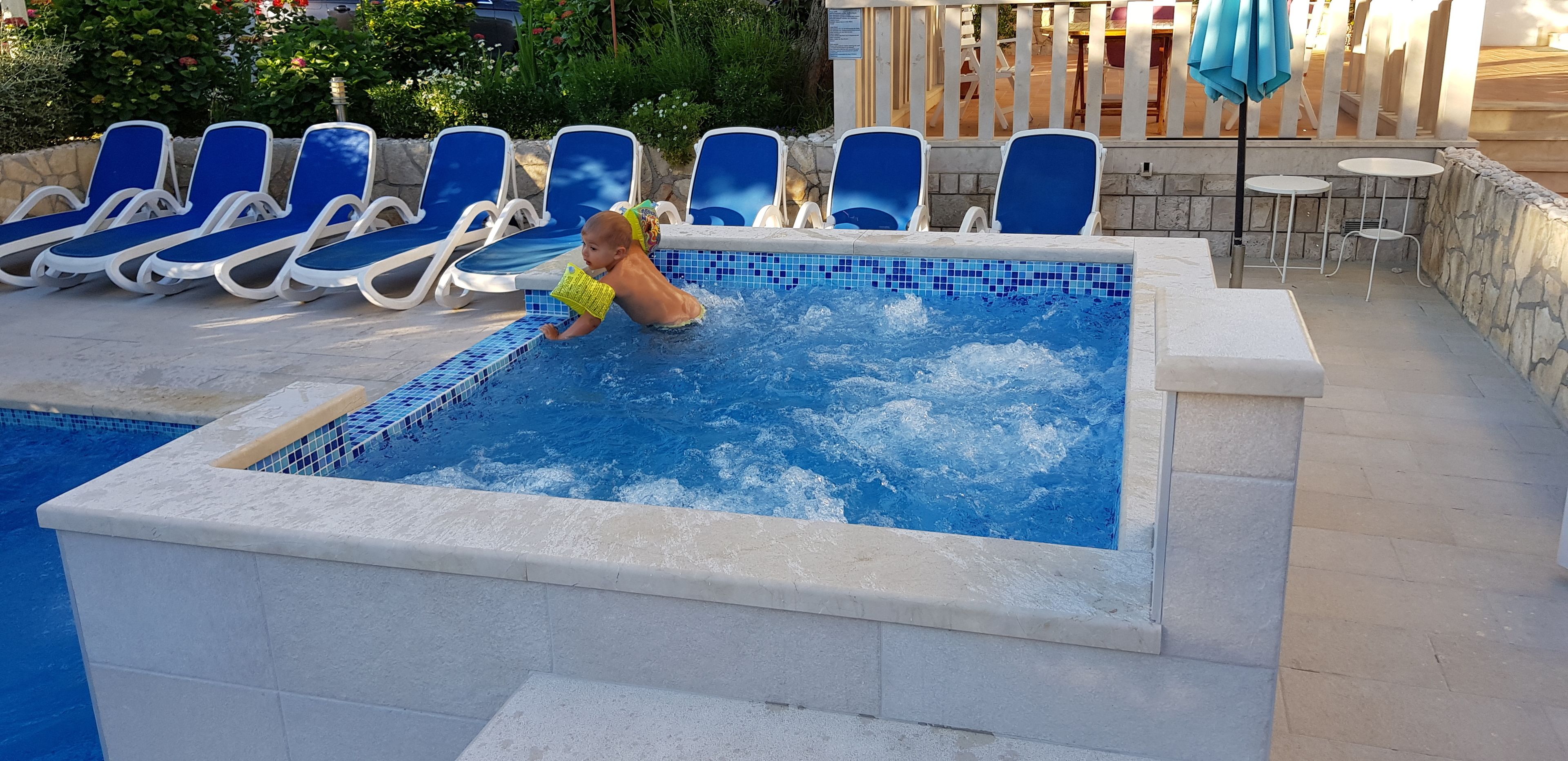 A pool area with blue lounge chairs and a hot tub.