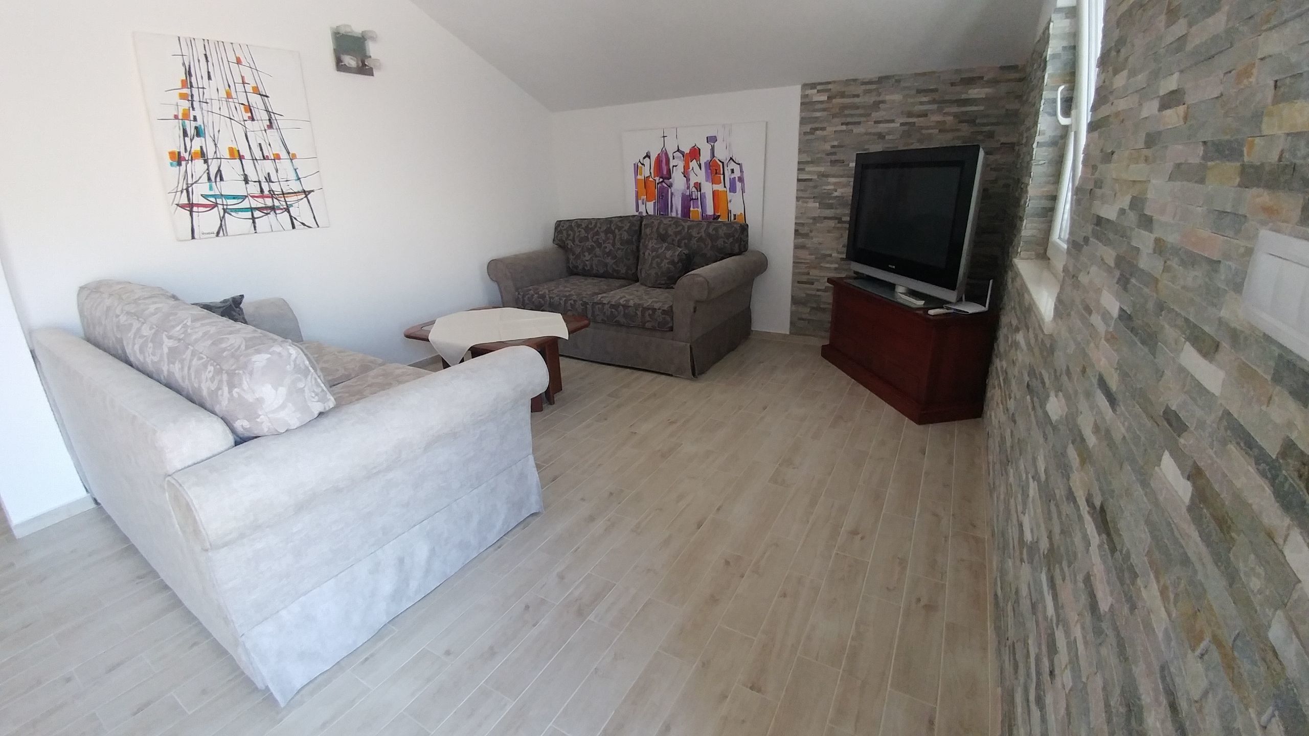 Un soggiorno con un divano, una poltrona, un tavolino e una TV su un mobile.