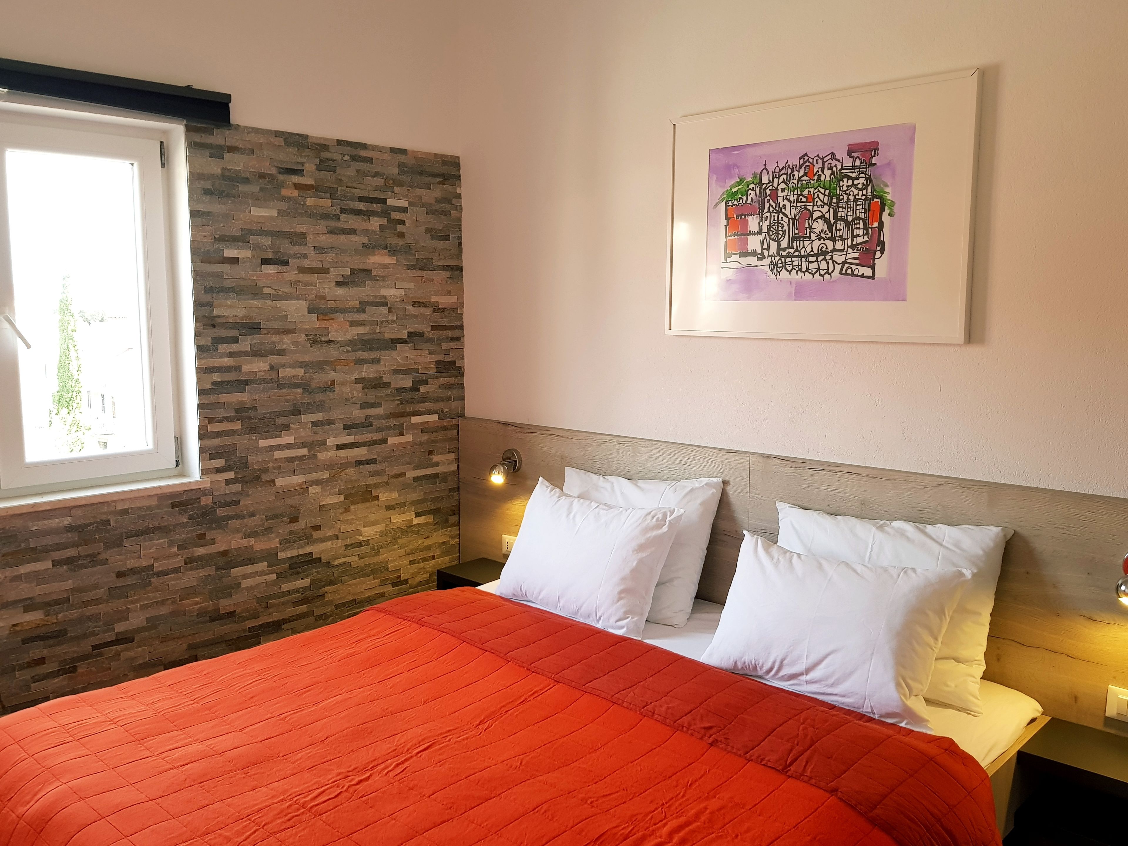 Ein Schlafzimmer mit einer Steinwand, einem großen Bett mit weißen Kissen, einem Fenster und einem gerahmten Bild an der Wand.