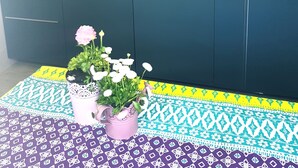 Cocina pequeña con microondas, lavamanos y armarios. Hay un mantel decorativo y una planta en maceta sobre la encimera.