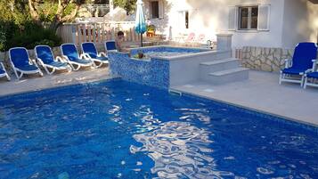 Una piscina con baldosas azules y un área de solárium con sillas reclinables también azules.