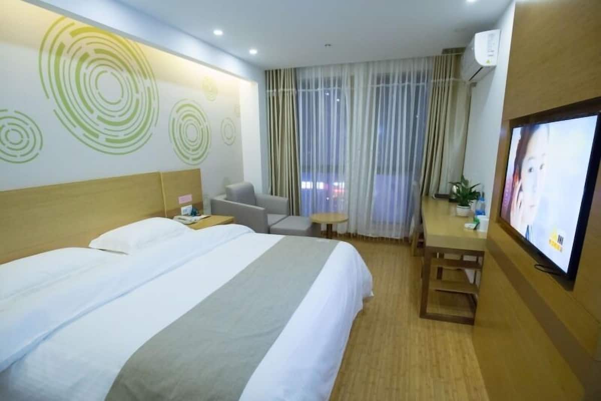 A hotel room with a large bed, a desk with a chair, a television, and a window with curtains.
