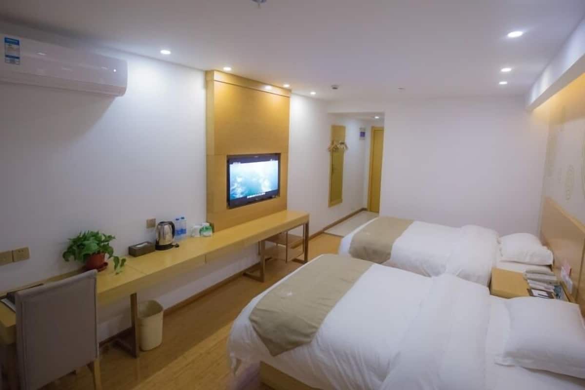 A hotel room with two beds, a desk, a television, and a mirror.