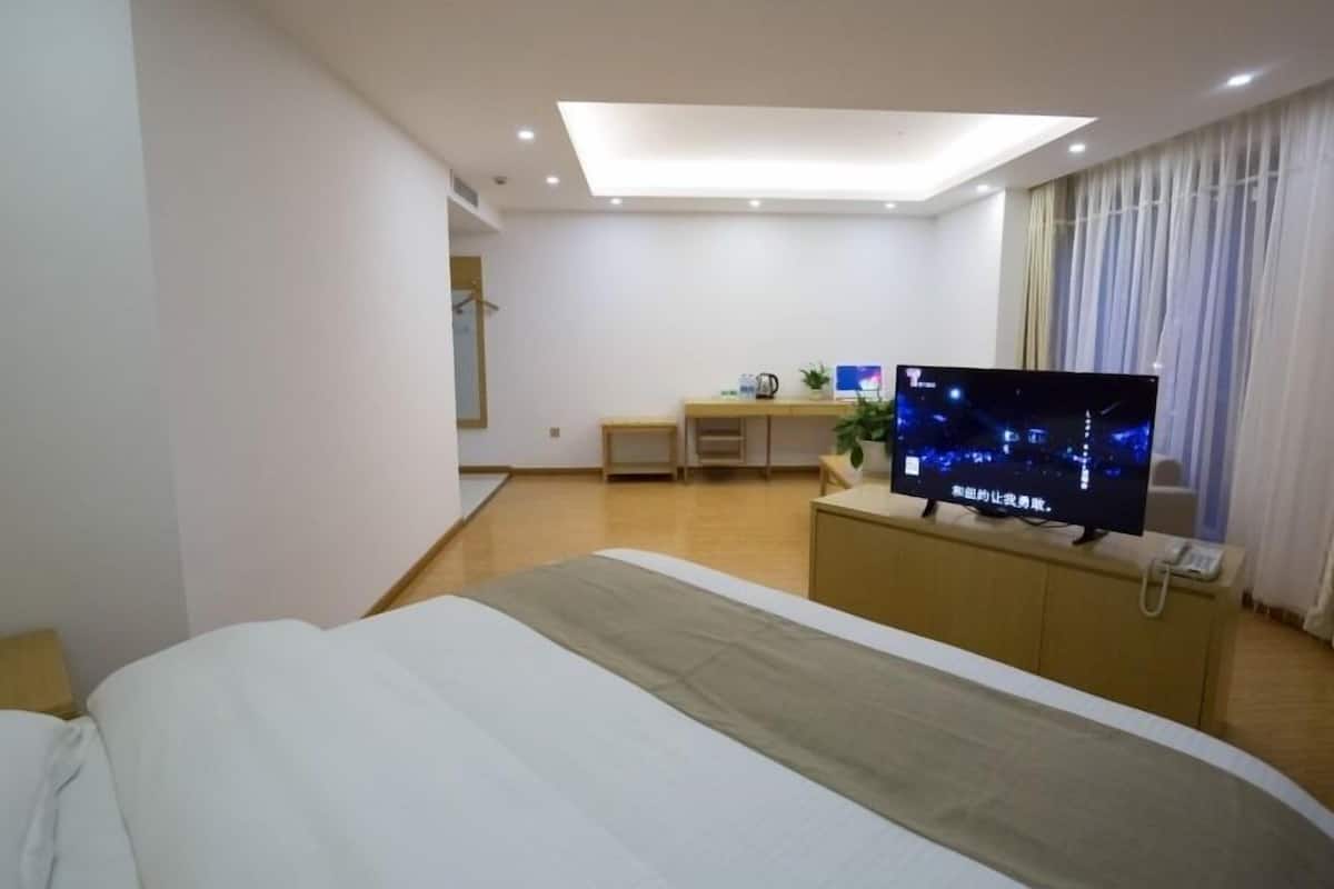 A hotel room with a bed, a desk, a television, and a window with curtains.